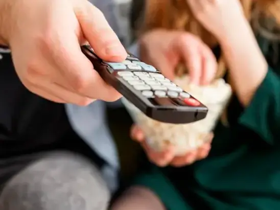 Mão segurando o controle remoto diante da TV