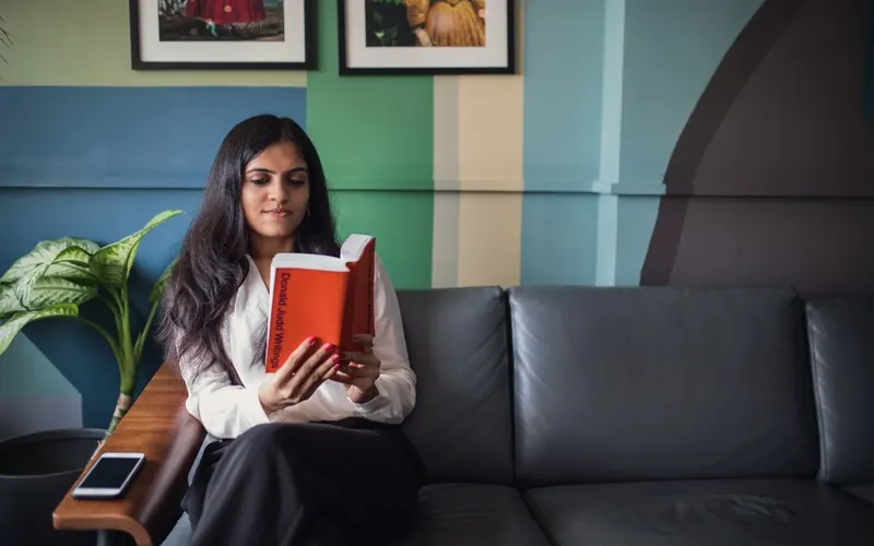 Mulher com celular e livros na sala